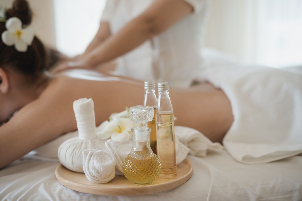 Bottle of essential oil on a wooden tray. background Young beautiful Asian woman relaxing in the spa massage